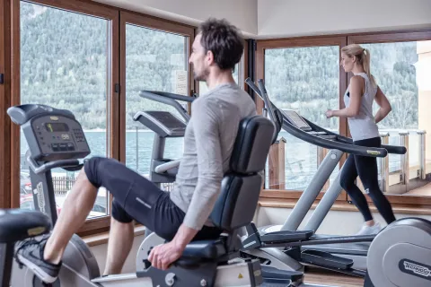 Mann und Frau beim Trainieren im Fitnessraum mit großen Glasfassaden und Ausblick auf den Achensee