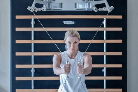 Blonde Frau beim Trainieren im Fitnessraum mit Seilzug an einer Sprossenwand