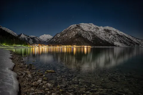 Blick vom Ufer auf den winterlichen Achensee in einer sternenklaren Nacht