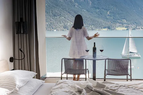 Frau steht in einem weißen Kleid auf dem Balkon eines Hotelzimmers mit Blick auf den Achensee