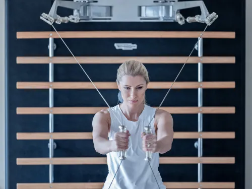 Blonde Frau beim Trainieren im Fitnessraum mit Seilzug an einer Sprossenwand