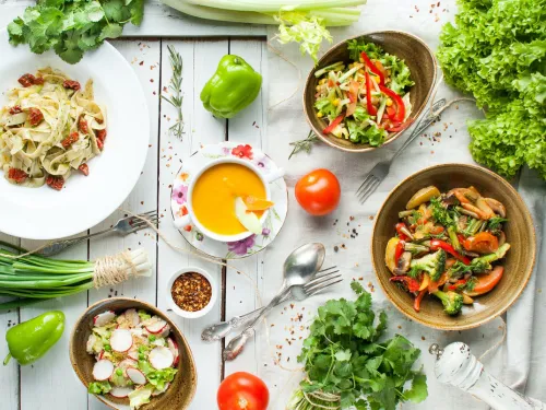 Vegane Gerichte mit buntem Gemüse und Salat auf einem weißen Holztisch