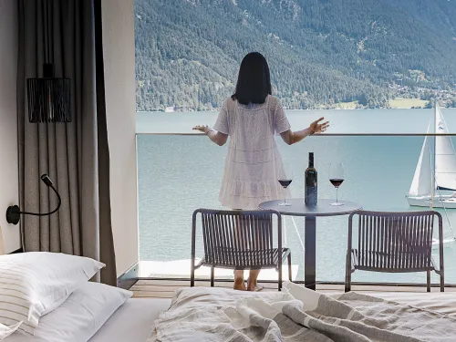 Frau steht in einem weißen Kleid auf dem Balkon eines Hotelzimmers mit Blick auf den Achensee